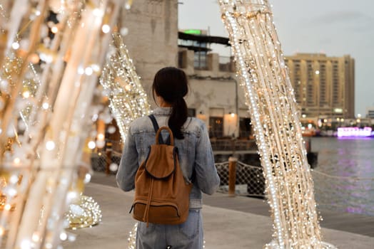 A young woman with a backpack on her back admires the architecture in the old Dubai Creek of Deira. Back view. Journey through the Persian Gulf