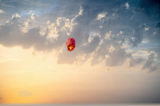 orange sky lantern floating in the middle of grey sky on the festival of independence day makar sankranti uttarayan India