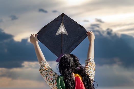 Young girl in traditional indian clothing holding black kite high above head launching it on sankranti republic independence day celebrations