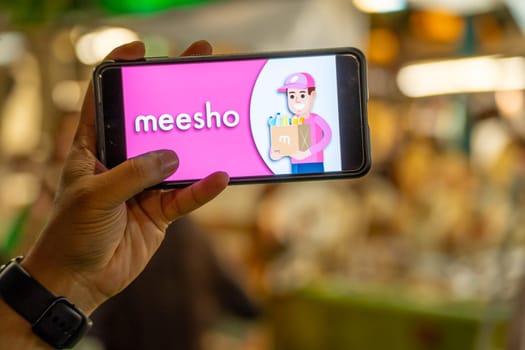 Delhi, India - 2nd Apr'23 : woman holding mobile phone showing indian social commerce startup Meesho logo at an event