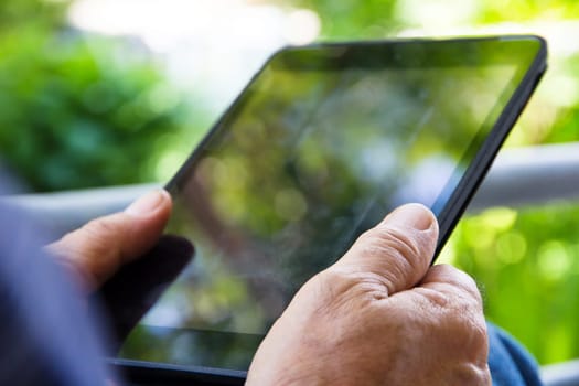 Senior man sitting outside reading E-book on his tablet.