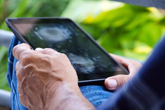 Senior man sitting outside reading E-book on his tablet.