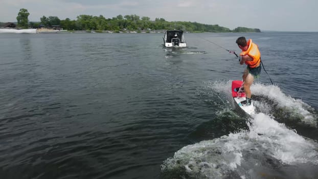 A young man gets up on a wakeboard. A sports guy rides on the water on the board. The boat rolls on the water. Back view. 4k