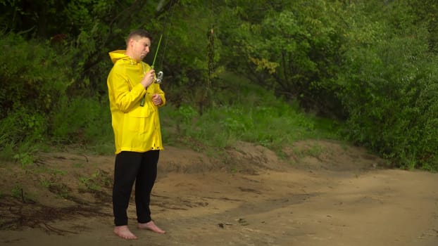 A young man in a yellow raincoat is fishing on the shore. The man caught seaweed on a hook and is crying. 4k