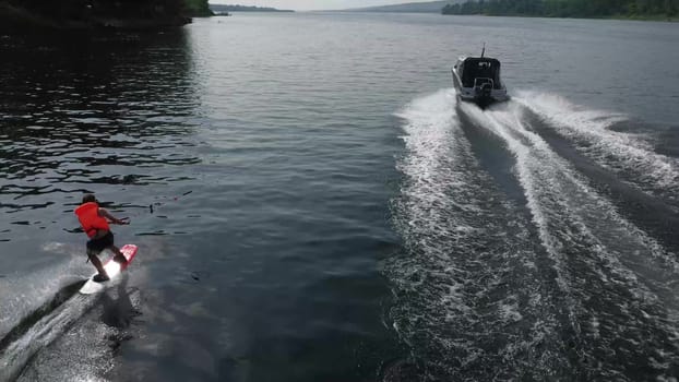 A young man rides a wakeboard. A sports guy rides on the water on a board behind a boat. Top view from a drone. 4k