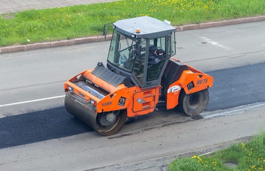 11.06.2022. Kemerovo, Russia. Road works on asphalt laying. Workers in vests are laying patches and rolling them out with a large roller.