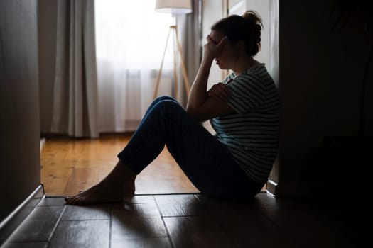Silhouette of sad and depressed woman sitting on the floor at home.