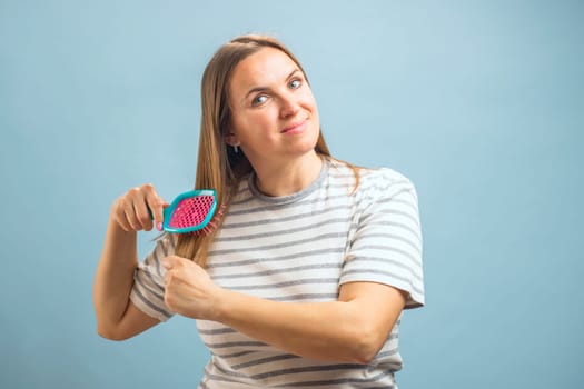 Beautiful brown-haired woman brushing her beautiful shiny hair with hairbrush on blue background