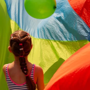 Little girl in striped T-shirt from back with long braid. With green balloon.On bright colored