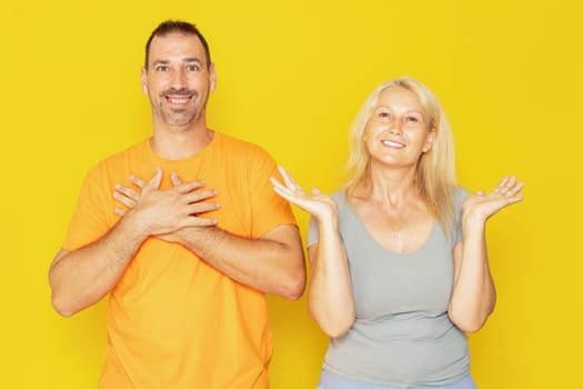 Caucasian couple in their 40s receiving amazing news that shocks them, isolated on yellow studio background