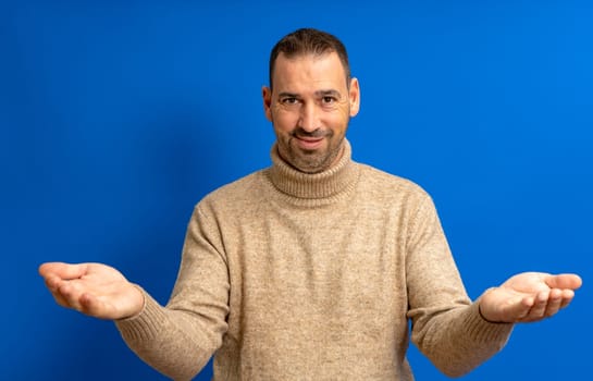 Bearded hispanic man in his 40s over blue background looking at the camera smiling with open arms for a hug. Cheerful expression embracing happiness.