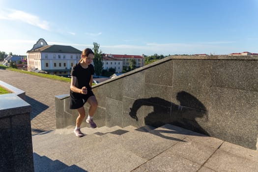 A young woman in black clothes running on stairs at city street early morning.