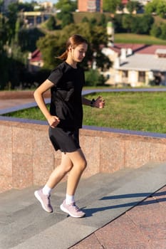 A young woman in black clothes running on stairs at city street early morning.