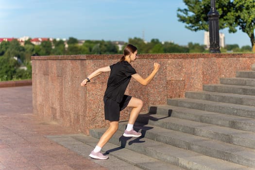 A young woman in black clothes running on stairs at city street early morning.