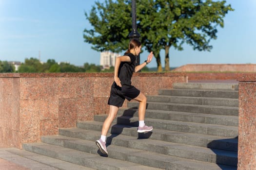 A young woman in black clothes running on stairs at city street early morning.