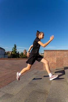 A young woman in black clothes running on stairs at city street early morning.