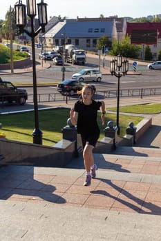 A young woman in black clothes running on stairs at city street early morning.