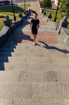 A young woman in black clothes running on stairs at city street early morning.