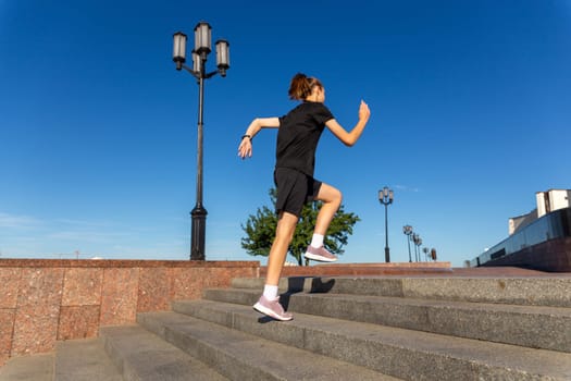 A young woman in black clothes running on stairs at city street early morning.