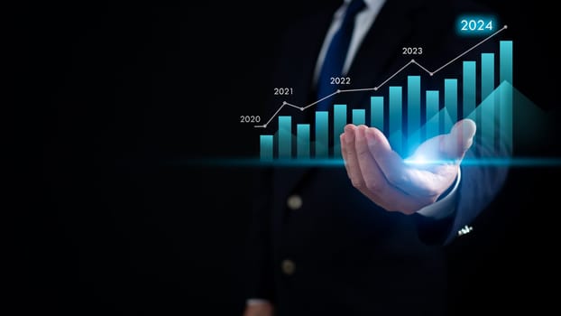 Stock trading. Finance. Investing. Growing business. Businessman in a suit is holding a virtual graph It represents growth of stocks and business in 2024.