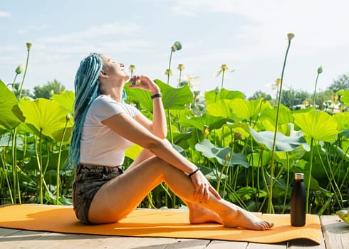 young beautiful woman with blue afro locks resting on yoga mat on wooden pierce on lotus lake enjoying nature