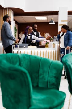 Young African American couple arriving at hotel, standing at reception with baggage talking with receptionist while checking in. Front desk agent getting information about guests during check-in