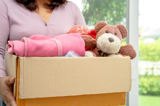 Holding clothing donation box with used clothes and doll at home to support help for poor people in the world.