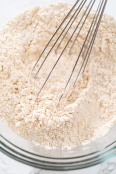 Mixing dry ingredients with a hand whisk in a large glass mixing bowl to bake mini Easter bread kulich.