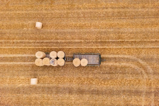 Hay bales stored on two trailers on a harvested agricultural field in summer, top view from drone perspective, Germany