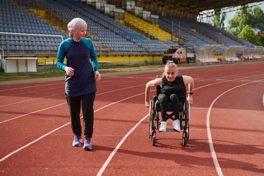 A Muslim woman in a burqa running together with a woman in a wheelchair on the marathon course, preparing for future competitions