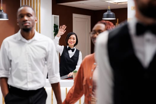 Happy receptionist waving at guests after doing check out process, wishing them a safe flight back home. Front desk employee saying goodbye to tourists after staying at luxury hotel.