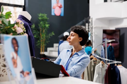 Stylish employee arranging blue shirt on mannequin, preparing boutique for customers. Caucasian woman with short hair working with fashionable merchandise in clothing store. Fashion concept