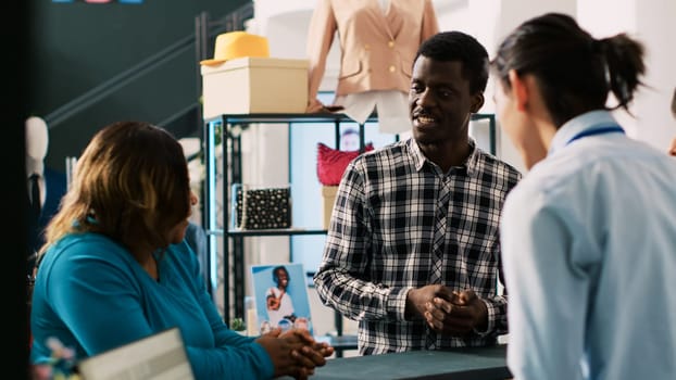 African american couple taking carton box with fashionable clothes, standing at store counter desk in modern boutique. Customers discussing online order price with stylish employee. Fashion concept