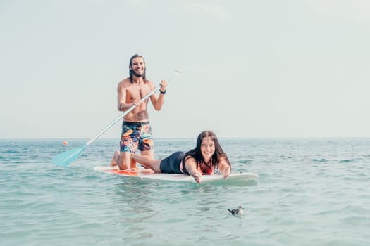 Sea woman and man on sup. Silhouette of happy young woman and man, surfing on SUP board, confident paddling through water surface. Idyllic sunset. Active lifestyle at sea or river