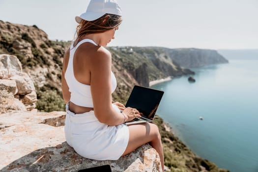 Digital nomad, Business woman working on laptop by the sea. Pretty lady typing on computer by the sea at sunset, makes a business transaction online from a distance. Freelance remote work on vacation