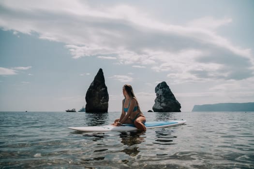 Close up shot of beautiful young caucasian woman with black hair and freckles looking at camera and smiling. Cute woman portrait in a pink bikini posing on a volcanic rock high above the sea