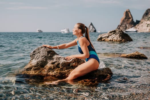 Woman travel sea. Young Happy woman in a long red dress posing on a beach near the sea on background of volcanic rocks, like in Iceland, sharing travel adventure journey