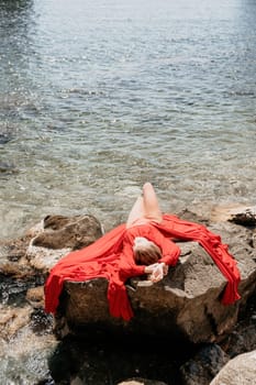 Woman travel sea. Young Happy woman in a long red dress posing on a beach near the sea on background of volcanic rocks, like in Iceland, sharing travel adventure journey