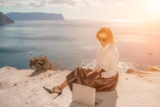 Freelance women sea. She is working on the computer. Good looking middle aged woman typing on a laptop keyboard outdoors with a beautiful sea view. The concept of remote work