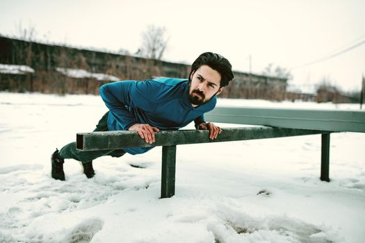 Young man athlete doing push ups and doing exercises during the winter training outside in while it snowing. Copy space.