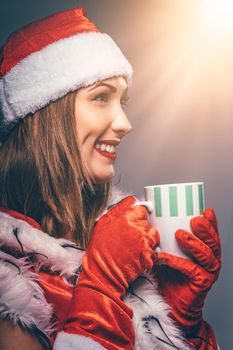 Portrait of a beautiful young smiling woman in Santa Claus costume. She is smiling and holding cup of hot tea.