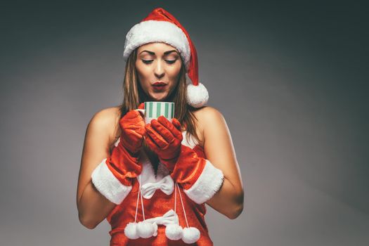 Portrait of a beautiful young smiling woman in Santa Claus costume. She is thinking and holding cup of hot tea.