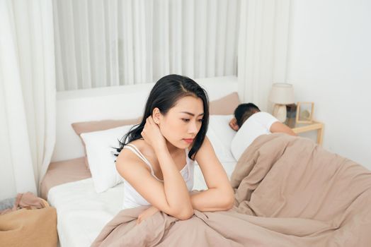 We have a problem. Young upset girl sitting on the edge of the bed, against her boyfriend, lying in bed.