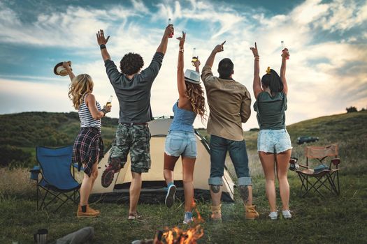 Happy young friends enjoy a nice day in nature. They're looking at sunset and greeting, happy to be together.