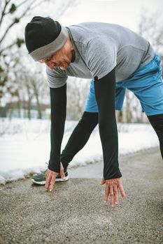 Active senior man stretching and doing exercises in public park during the winter training outside in.