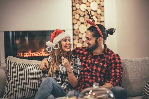 Cute beautiful couple is spending New Year eve at home sitting on sofa. They have great holidays having fun in nice company indoors. 