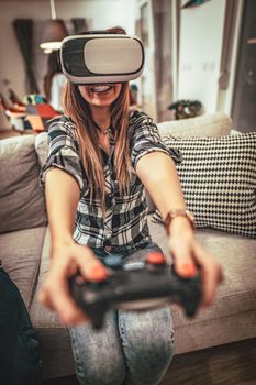 Happy young woman is playing video games with virtual reality glasses. She is having fun with new technology console online.