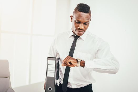 Successful African businessman is looking at his watch in modern office, not to be late.