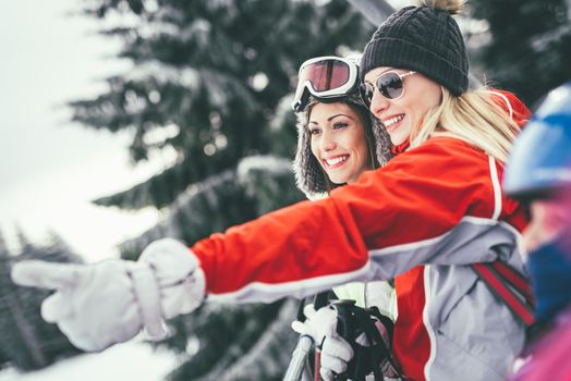 Beautiful young woman friends enjoying in winter vacations. They driving on ski lift and looking away with smile.