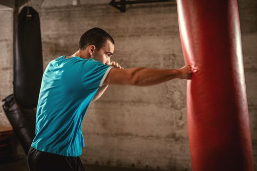 Young muscular man punching a boxing bag on cross fit training at the gym.